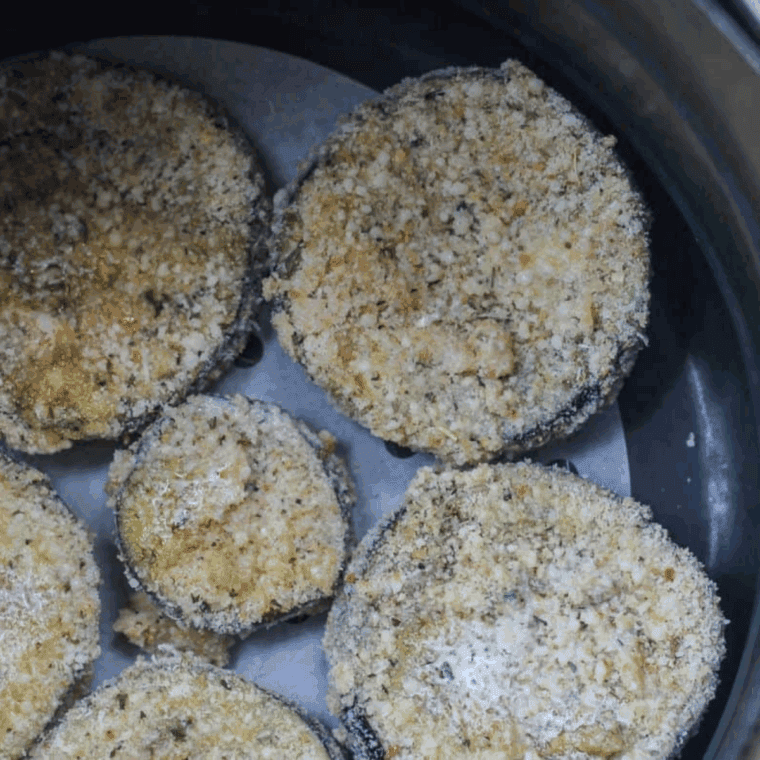 Breaded eggplant slices cooking in air fryer basket