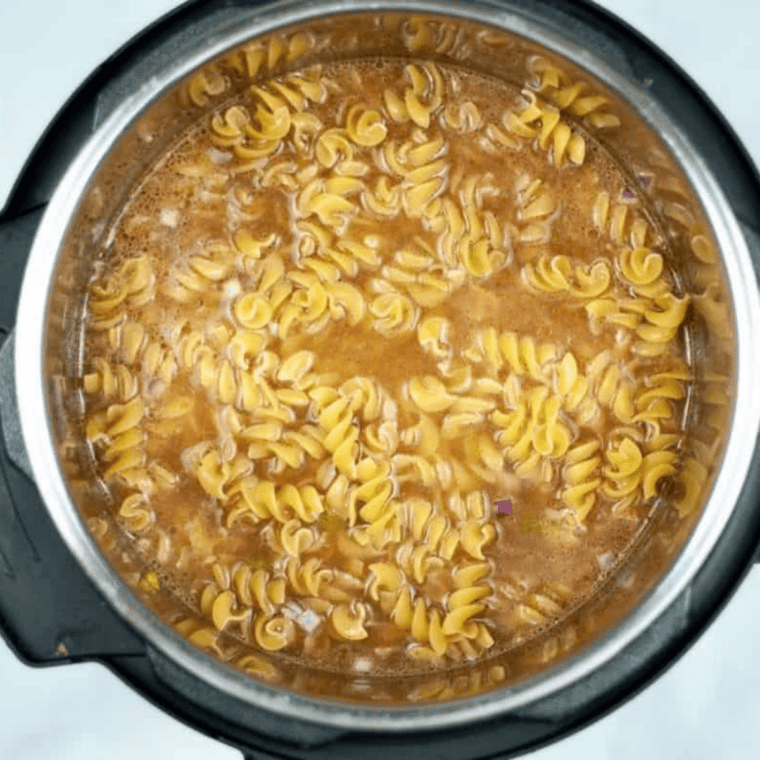Uncooked rotini pasta layered on top of liquid in the Instant Pot before pressure cooking.
