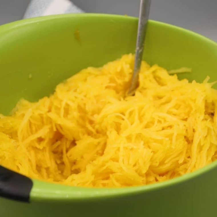 Spoon lifting seeds and pulp from the center of a cooked spaghetti squash