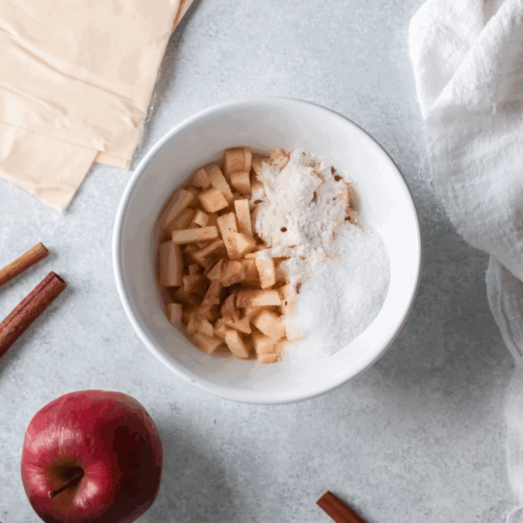 Mixing diced apples with brown sugar, cinnamon, nutmeg, lemon juice, and cornstarch in a bowl for apple turnover filling