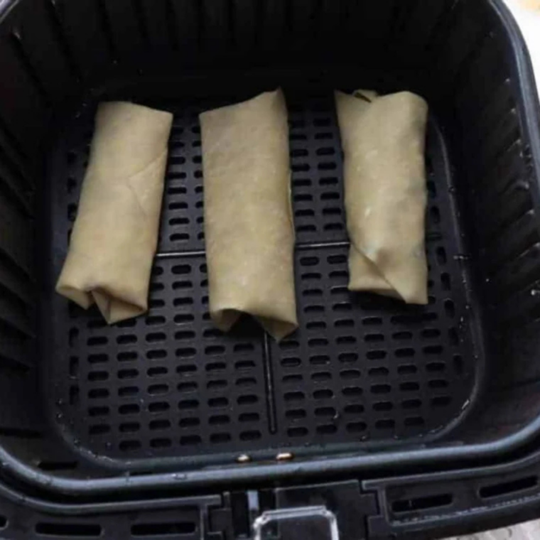 Cookie dough egg rolls arranged seam side down in a single layer in an air fryer basket
