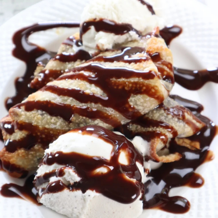 Golden crispy air fryer cookie dough egg rolls dusted with powdered sugar and served with vanilla ice cream