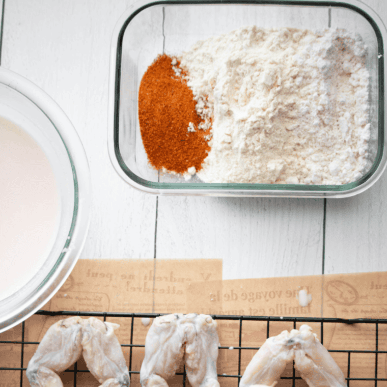 Coated frog legs arranged in a greased air fryer basket, cooking at 400&deg;F until golden brown and crispy, flipped halfway through.