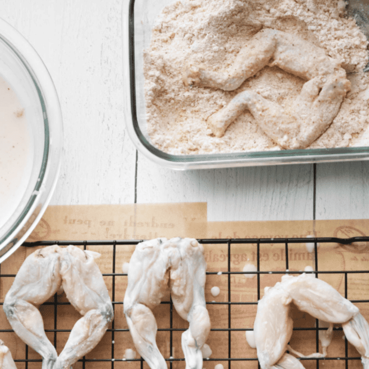 Frog legs in the air fryer being sprayed with cooking oil to achieve a golden, extra-crispy exterior.