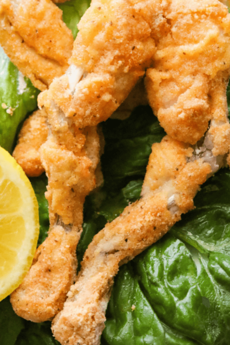 Golden-brown, crispy frog legs cooked in an air fryer, served on a plate with herbs.