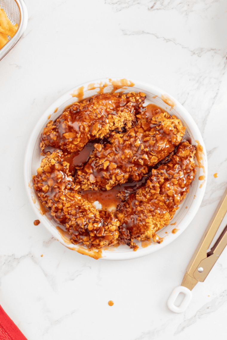 Golden crispy air fryer chicken tenders brined in pickle juice served with dipping sauce on a plate.