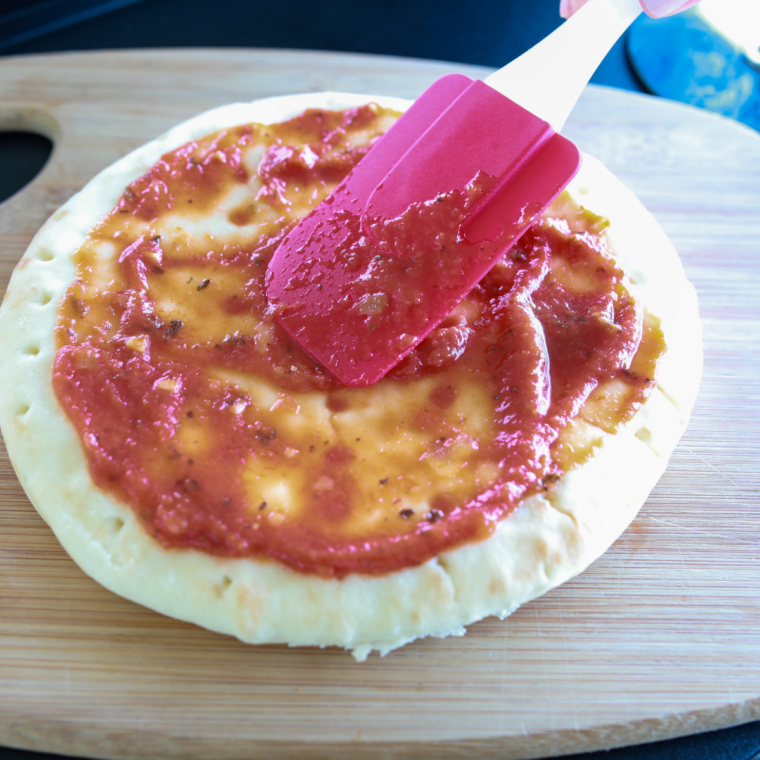 Spreading pizza sauce and mozzarella on crust for Blackstone pepperoni pizza