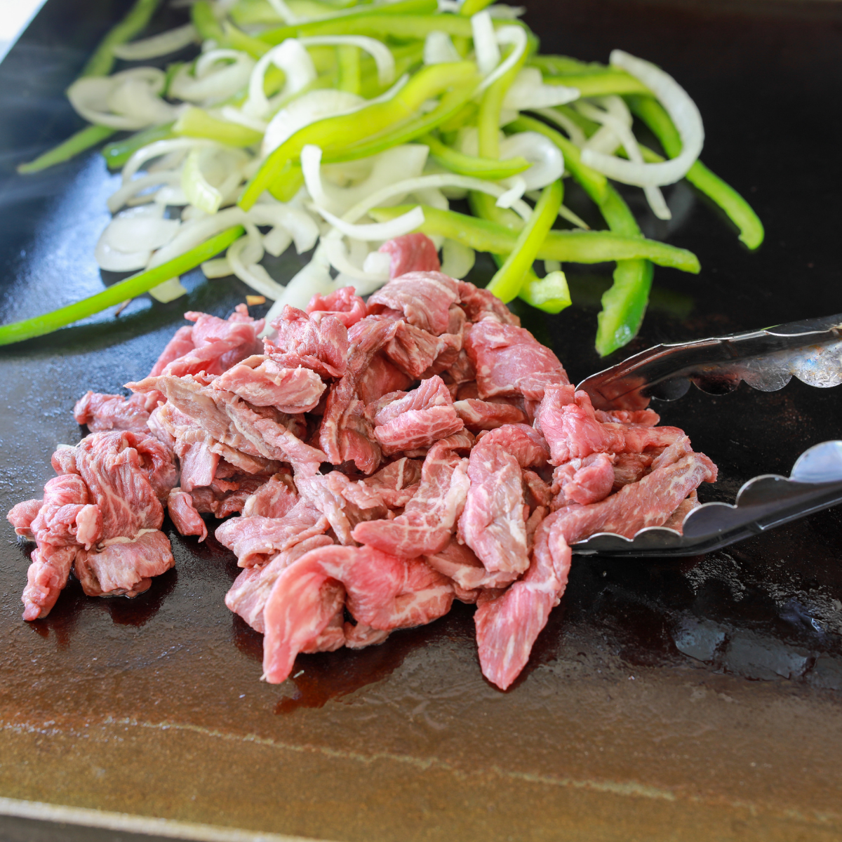 Ribeye steak sizzling on a Blackstone griddle while being chopped and folded with a metal spatula.