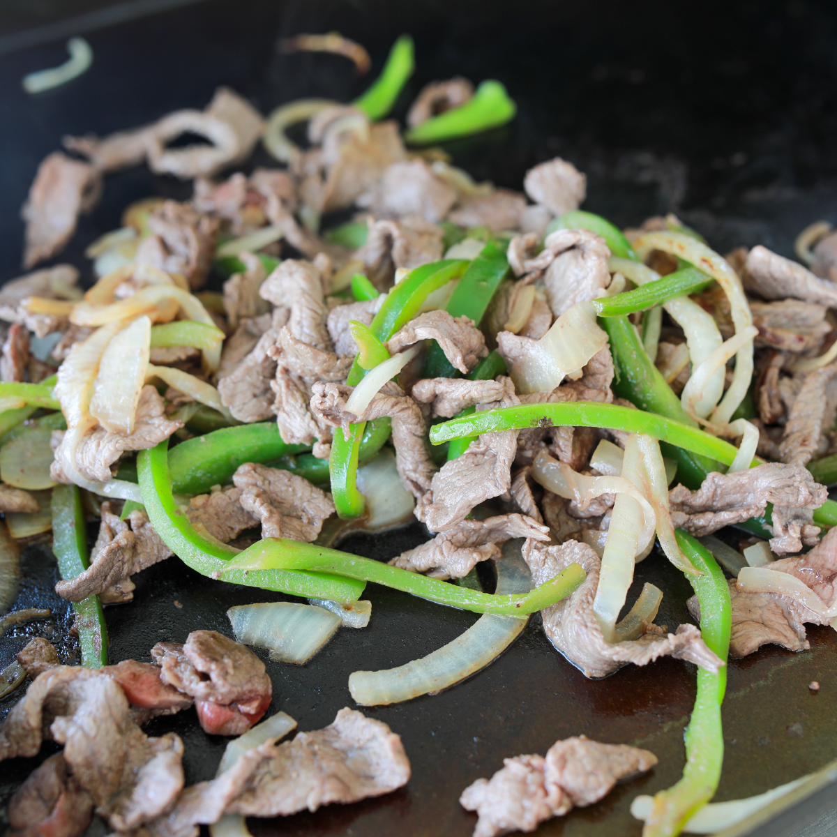 Onions, peppers, and mushrooms cooking on a Blackstone griddle next to chopped ribeye steak