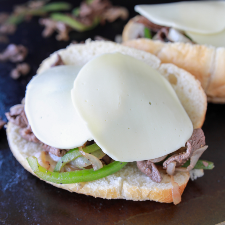 Melted provolone cheese covering steak and vegetable mixture on a Blackstone flat-top griddle.