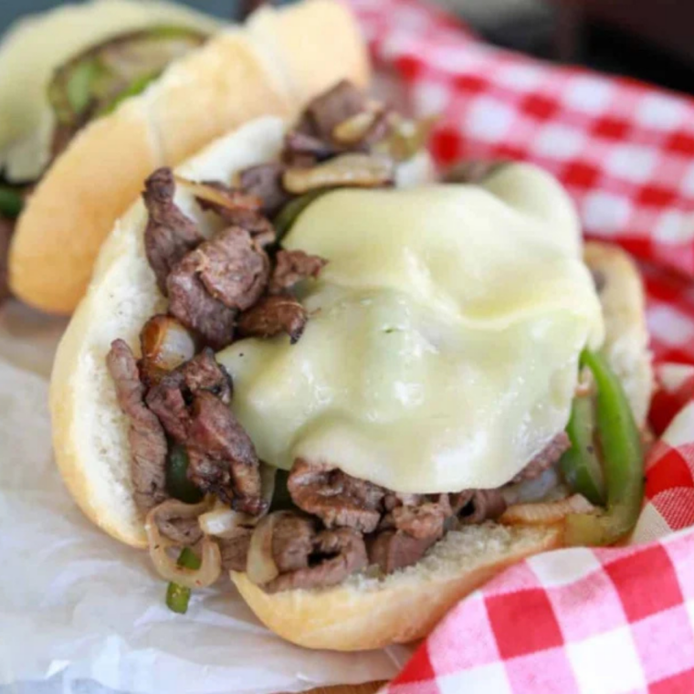 Toasted hoagie roll being filled with cheesy Philly cheesesteak mixture directly from the Blackstone griddle.