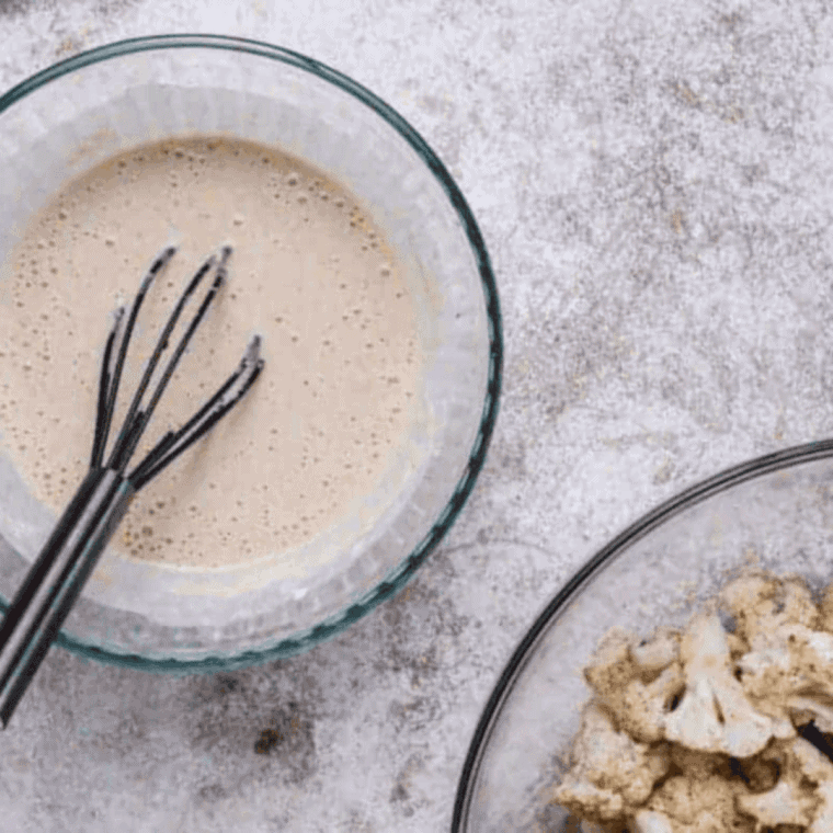 Cooking minced garlic in olive oil, butter, hot sauce, and lime juice in a saucepan to make spicy Buffalo sauce for cauliflower bites.