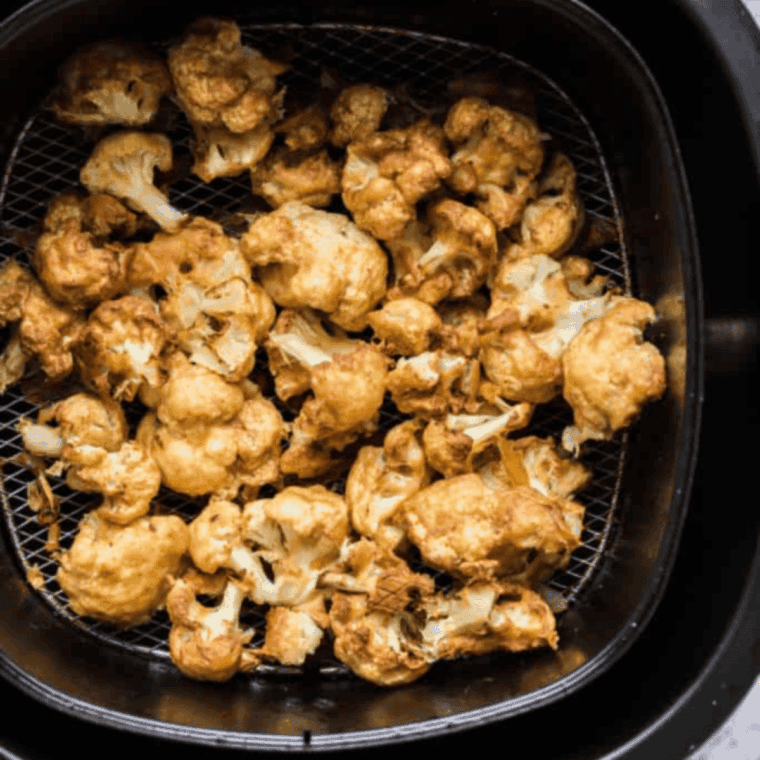 Cauliflower florets arranged in a single layer in an air fryer basket, ready to cook at 400°F for crispy Buffalo cauliflower bites.”