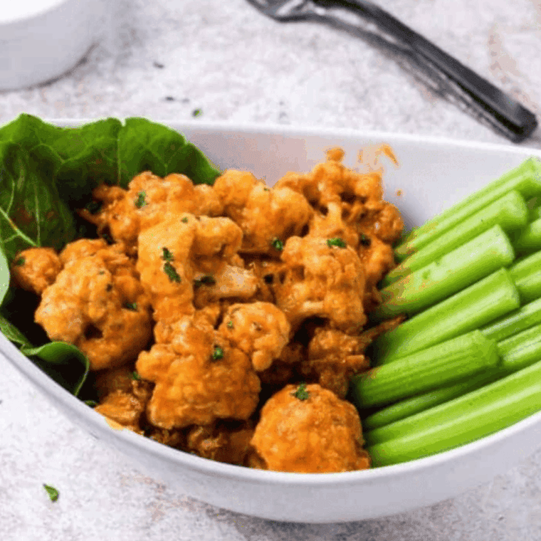 Crispy Buffalo Wild Wings–style cauliflower bites coated in spicy buffalo sauce, served with ranch dressing and celery sticks on a platter.