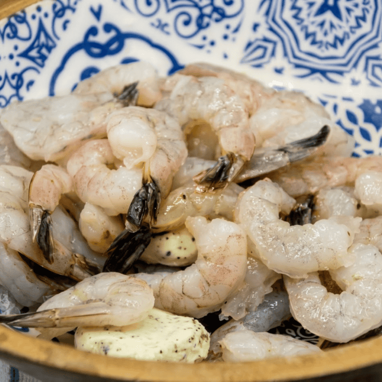 Raw shrimp in a large bowl coated with butter, Parmesan, garlic, parsley, lemon juice, salt, and pepper.