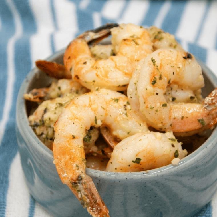 Shrimp coated in garlic parmesan mixture arranged in an air fryer basket ready to cook.