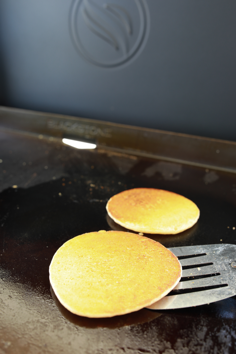 Stack of fluffy Blackstone griddle pancakes golden brown with butter melting and syrup dripping on top fresh off the griddle.