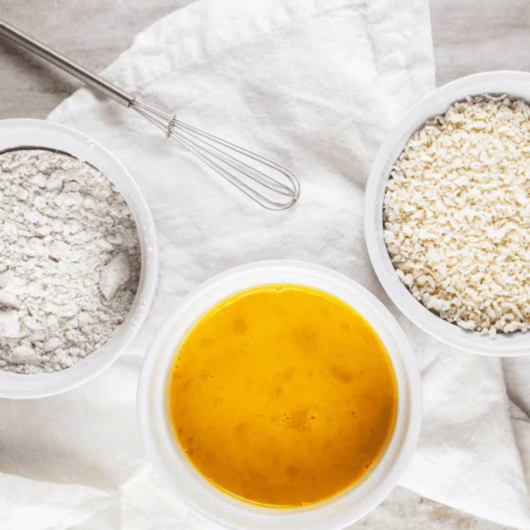 Three shallow bowls set up for breading shrimp with flour, beaten eggs, and seasoned breadcrumbs.