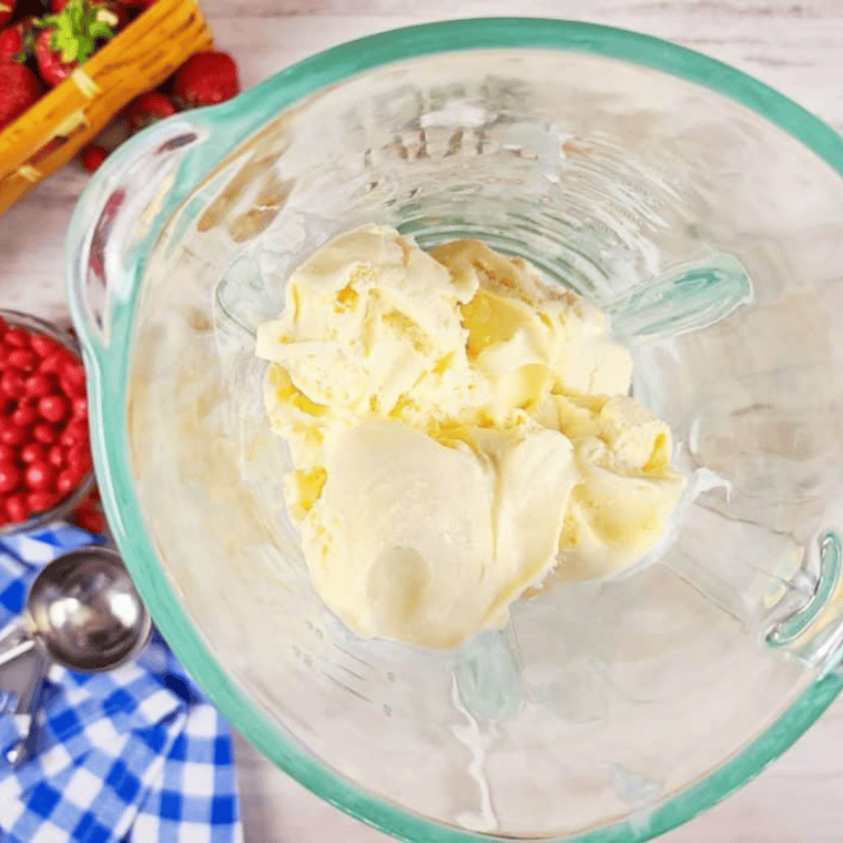 Blender filled with vanilla ice cream and crushed Skittles freeze pops being blended into a pink milkshake.