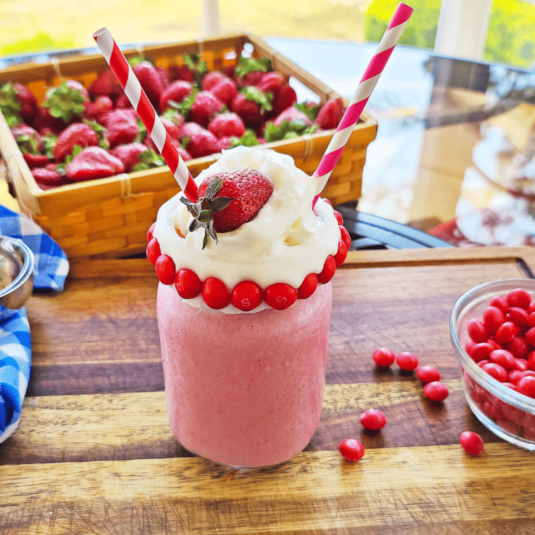 Pouring a pink strawberry Skittles milkshake into a glass rimmed with white chocolate and Skittles.
