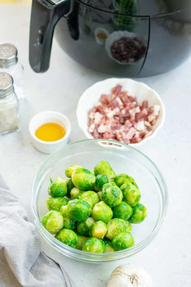 Ingredients for air fryer Brussels sprouts with bacon: halved Brussels sprouts, chopped bacon, garlic, honey, olive oil, salt and pepper