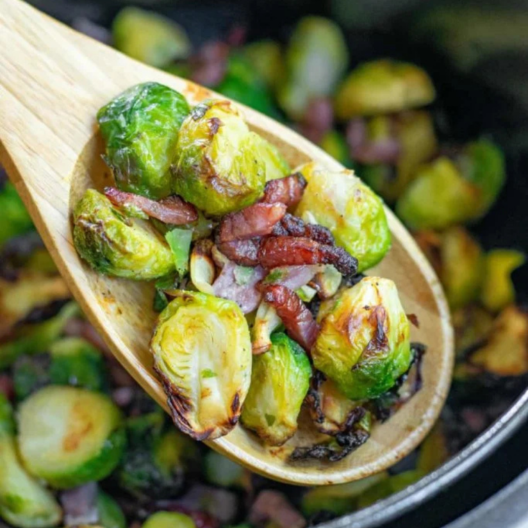 Honey being drizzled over half-cooked Brussels sprouts and bacon in the air fryer basket