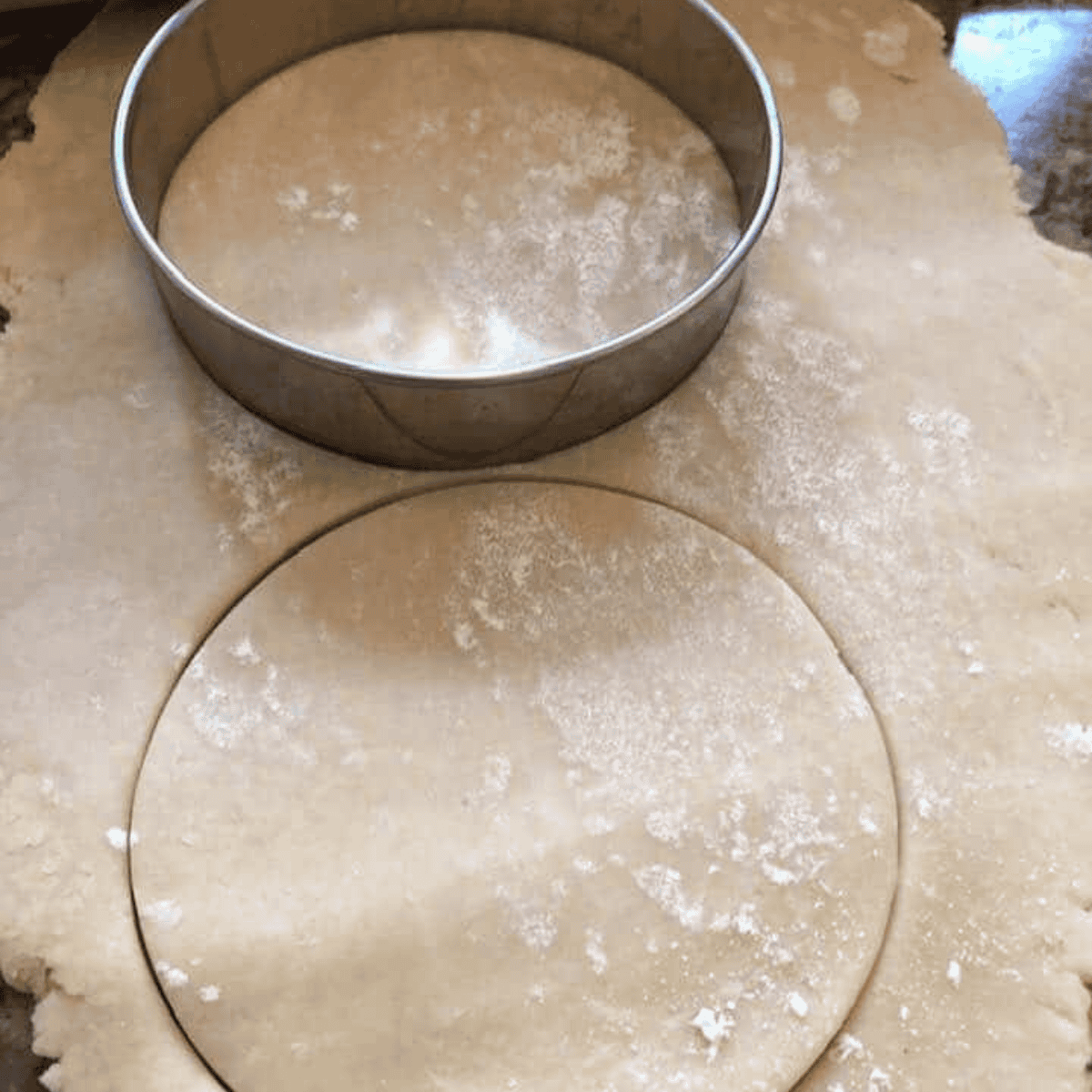 Rolling out pie crust on a floured surface and cutting circles with a round cutter for cherry hand pies