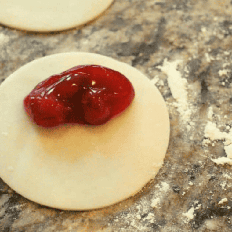 Spooning cherry filling onto dough circles and crimping the edges with a fork to seal the hand pies