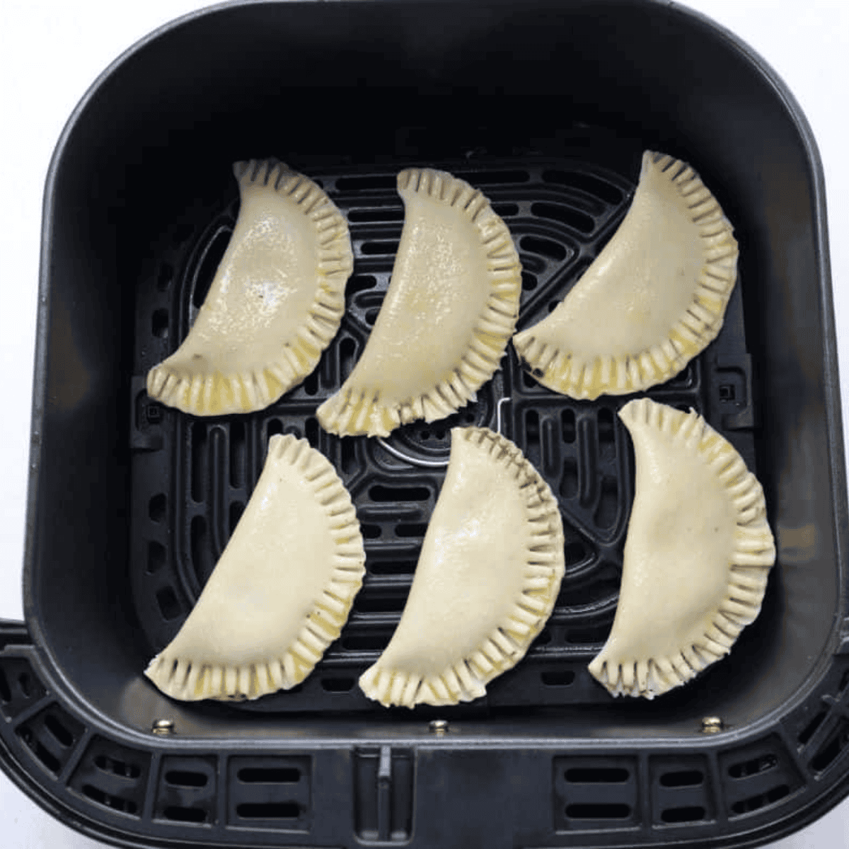 Uncooked cherry hand pies spaced apart in the air fryer basket before air frying