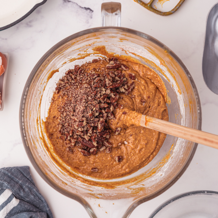 Chopped pecans being folded into pumpkin banana bread batter