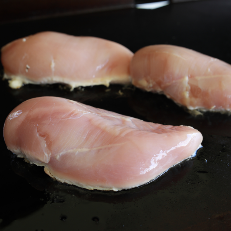 Prep the chicken: Boneless chicken breasts being sliced and pounded to an even thickness on a cutting board before seasoning.