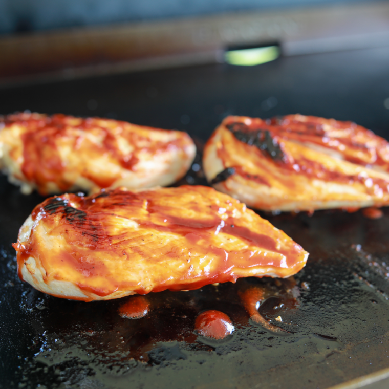 Griddle the chicken: Seasoned chicken breasts cooking on a hot Blackstone griddle with a golden crust forming on the surface.