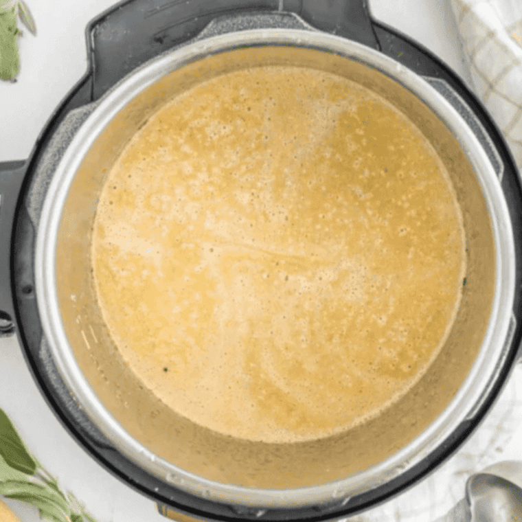 Immersion blender pureeing cooked butternut squash and sweet potato into smooth soup