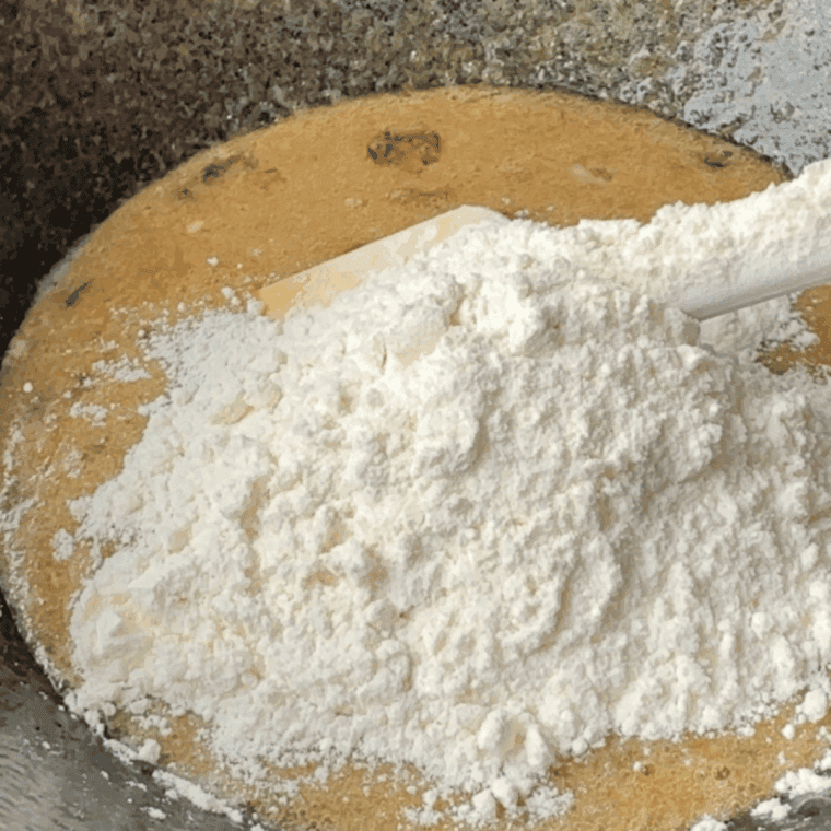 Whisking together flour, baking soda, and salt, then gradually mixing dry ingredients into the cookie dough.
