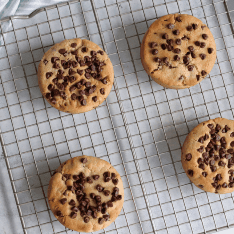 Freshly baked Copycat Otis Spunkmeyer Chocolate Chip Cookies stacked on a cooling rack with melted chocolate chips.