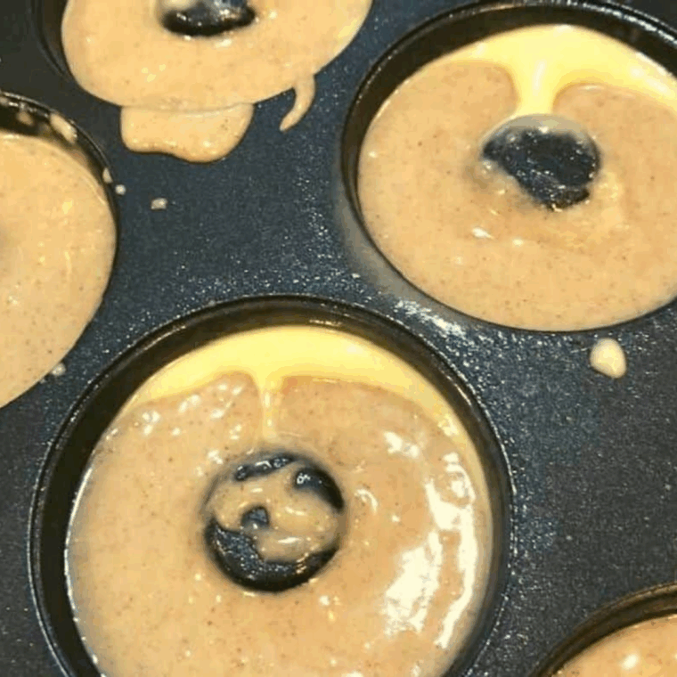 Pouring banana donut batter into a greased pan, filled two-thirds full.