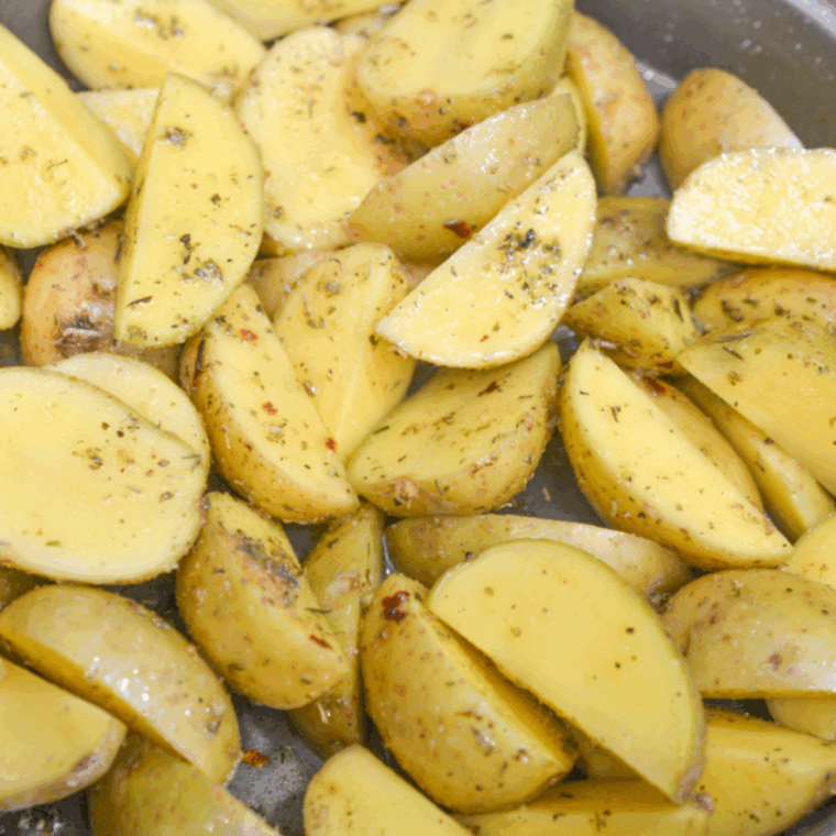 Baby potato halves coated in olive oil and seasoned with garlic powder, paprika, rosemary, salt, and pepper in a large mixing bowl.
