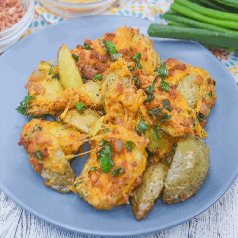 Crispy air fryer loaded baby potatoes topped with melted cheese, bacon bits, and chopped green onions in a serving bowl.