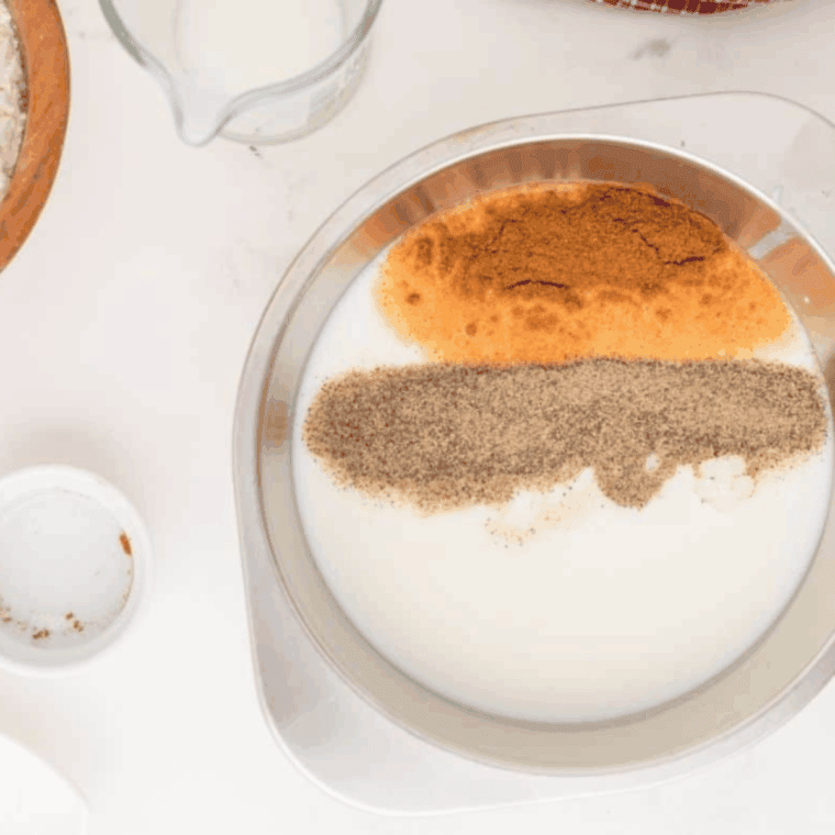 Raw chicken breasts marinating in a glass bowl with creamy buttermilk and spicy red hot sauce.