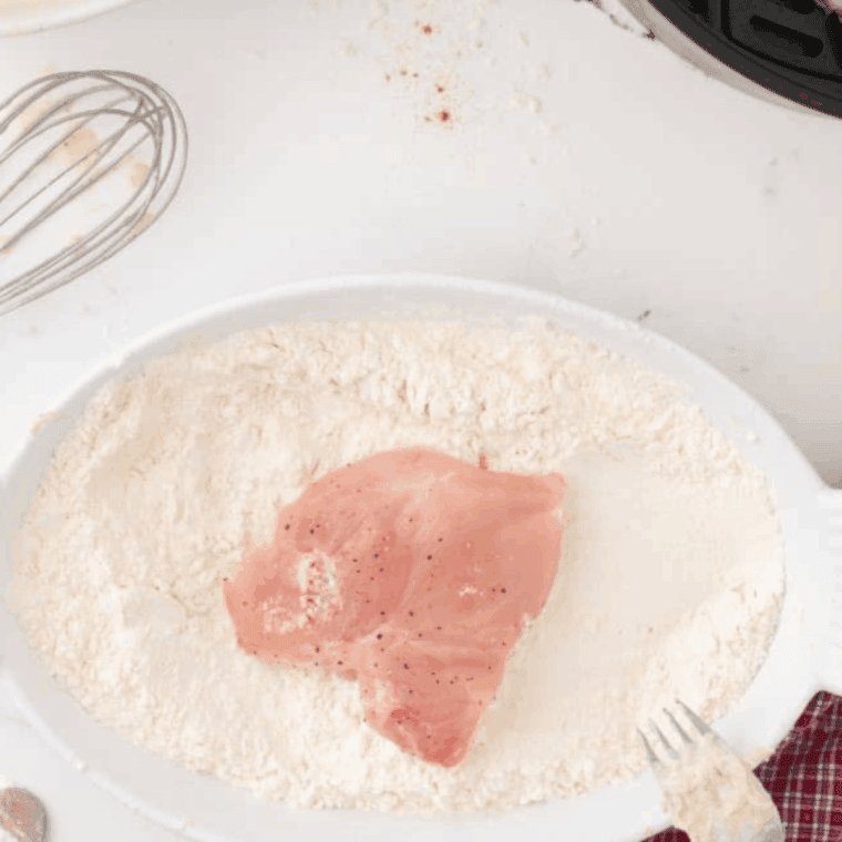 A shallow white bowl containing a mixture of flour, cornstarch, and orange-hued Cajun spices like paprika and cayenne.
