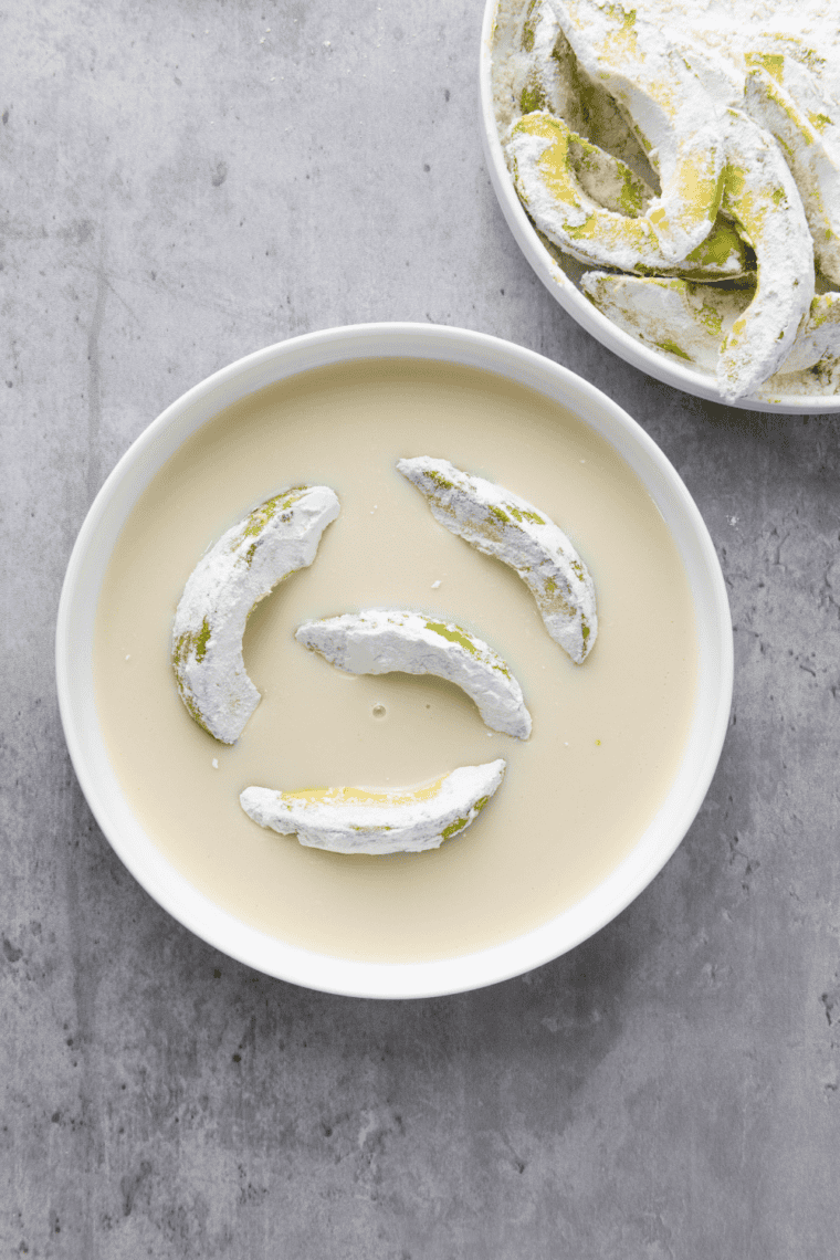 floured avocado fry being dipped in beaten egg and coated with breadcrumbs