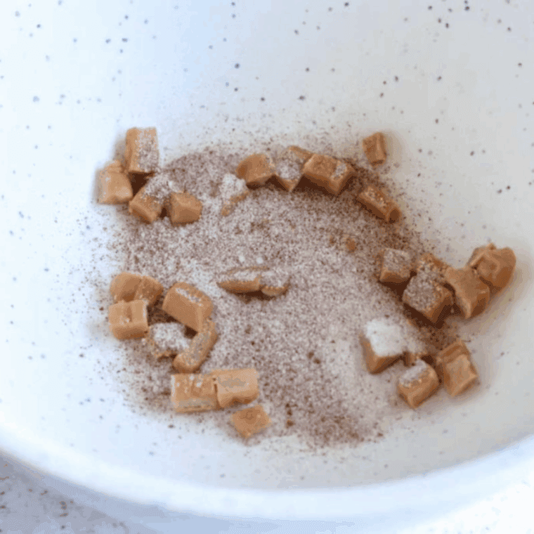 Chopped caramels and diced apples mixed with apple pie spice and sugar in a bowl.
