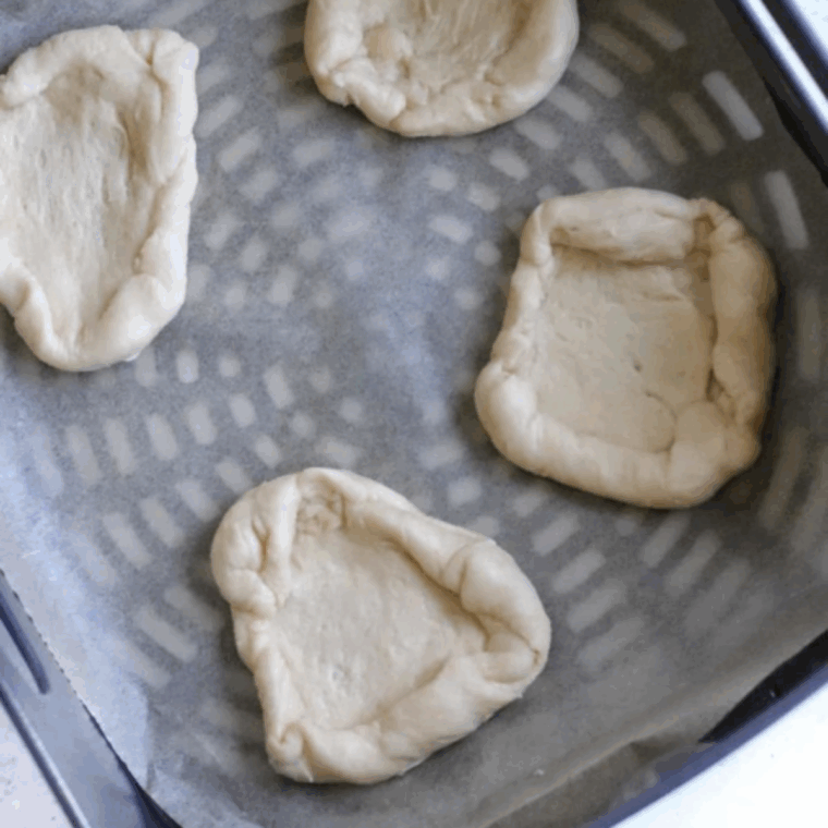 Crescent dough cut and shaped into round Danish pastries with edges rolled up, arranged on parchment paper in the air fryer basket.
