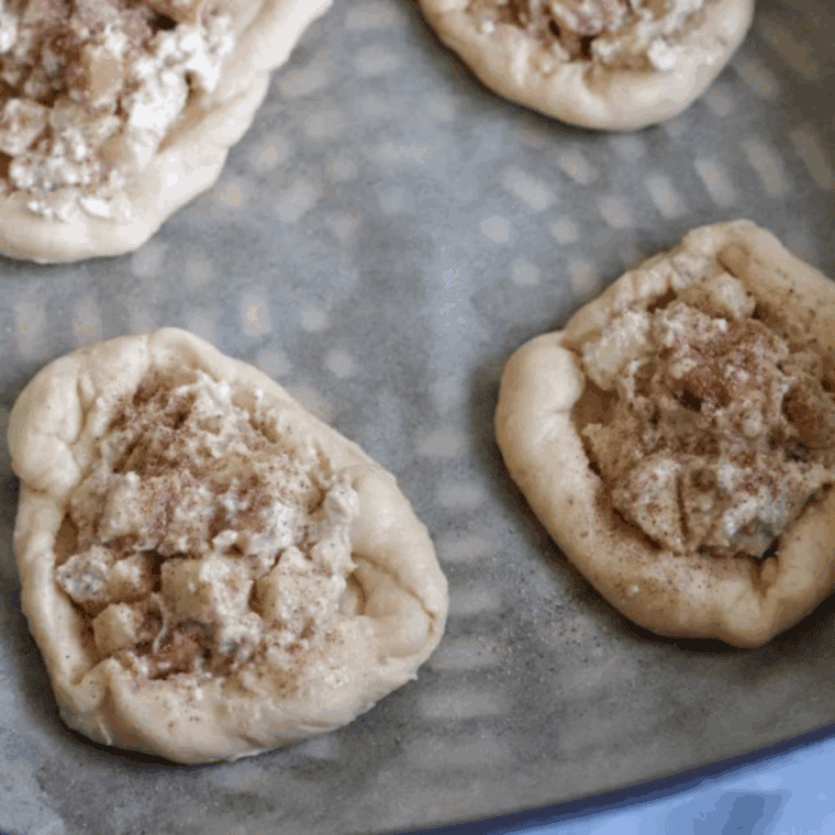 Crescent dough pieces shaped into round Danish pastries with edges rolled up, spaced evenly on parchment paper for air frying.