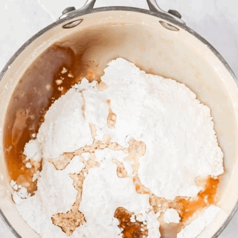 Whisking confectioner’s sugar, milk, maple syrup, and maple extract over medium heat to create smooth maple glaze.