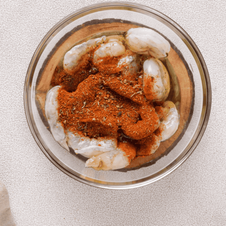 Tossing raw shrimp with Old Bay seasoning, olive oil, and lemon juice in a glass bowl