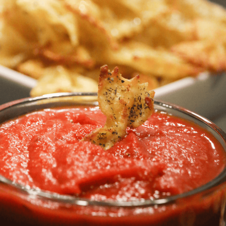 Close-up of crunchy bow tie pasta chips being dipped into a small ramekin of marinara sauce.