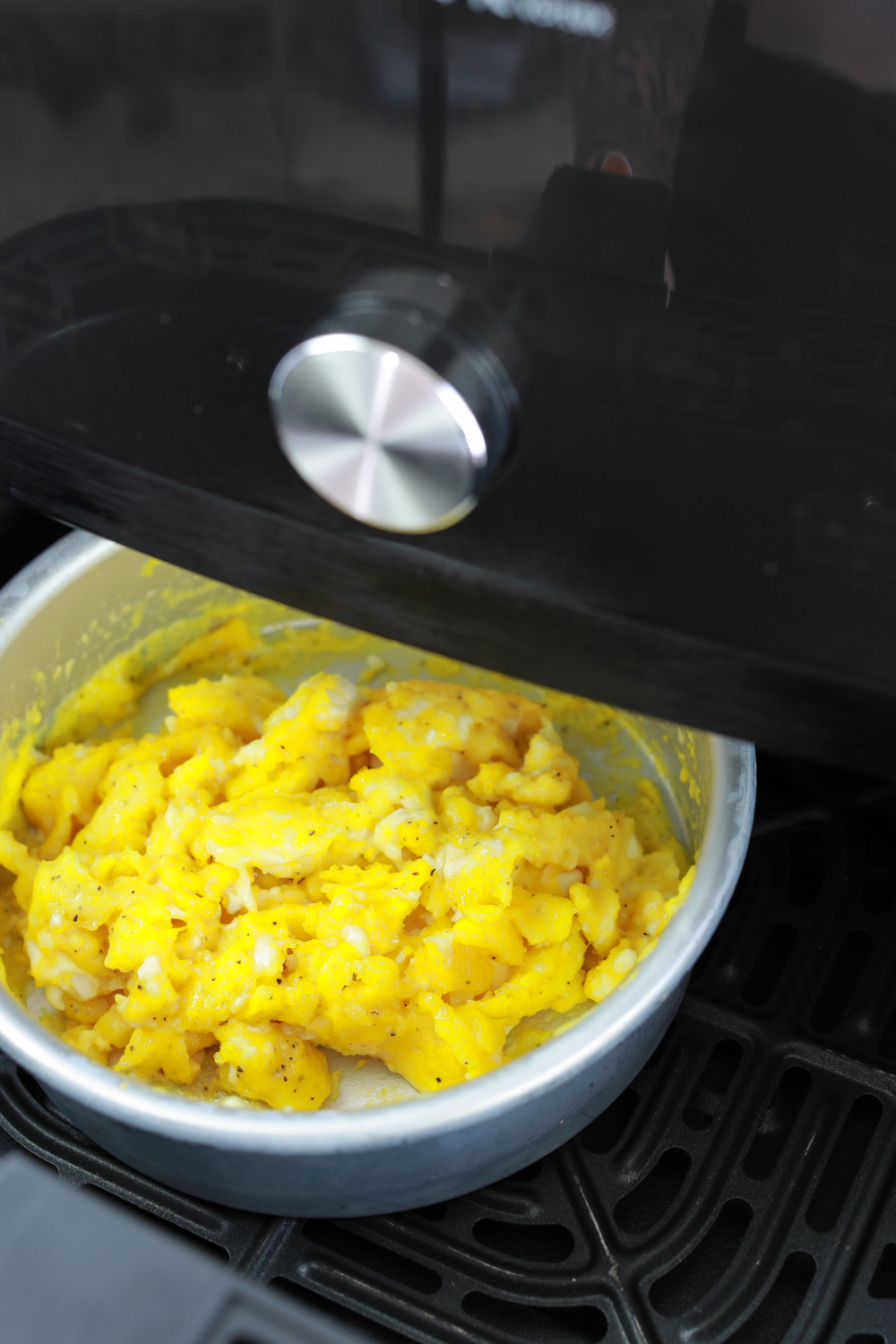 pouring whisked eggs into butter-coated pan inside air fryer basket before cooking.