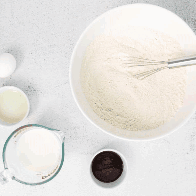 Greased donut pans ready, with flour, sugar, and baking powder mixed in a large bowl.