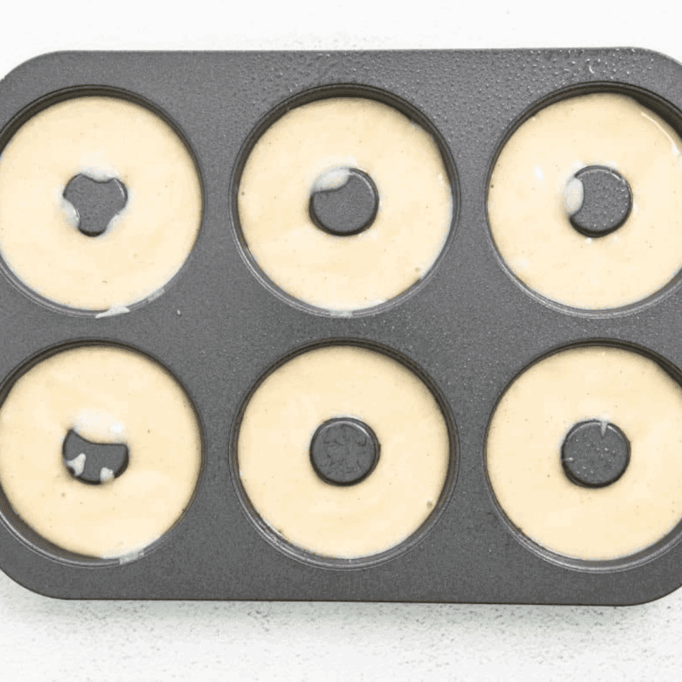 Pouring donut batter evenly into greased doughnut pans for baking.